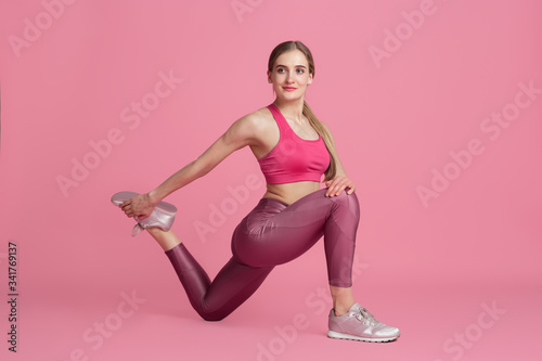 Stretching. Beautiful young female athlete practicing in studio, monochrome pink portrait. Sportive fit caucasian model training. Body building, healthy lifestyle, beauty and action concept.