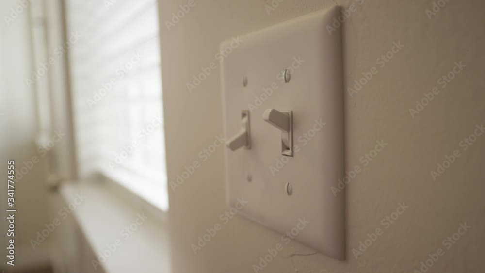 A person turn a light switch on during the day inside a home