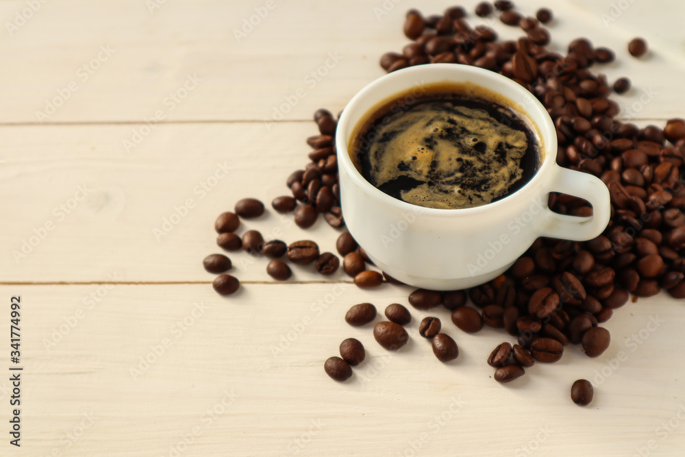 Cup with tasty coffee and roasted grains on wooden table