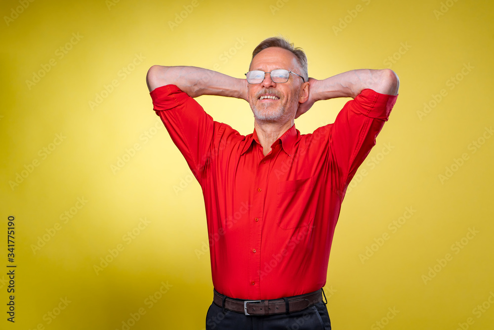 Aged, senior man is standing with hands over head. Relaxed. Isolated against yellow background Aged, senior man is standing with hands over head. Relaxed. Isolated against yellow background