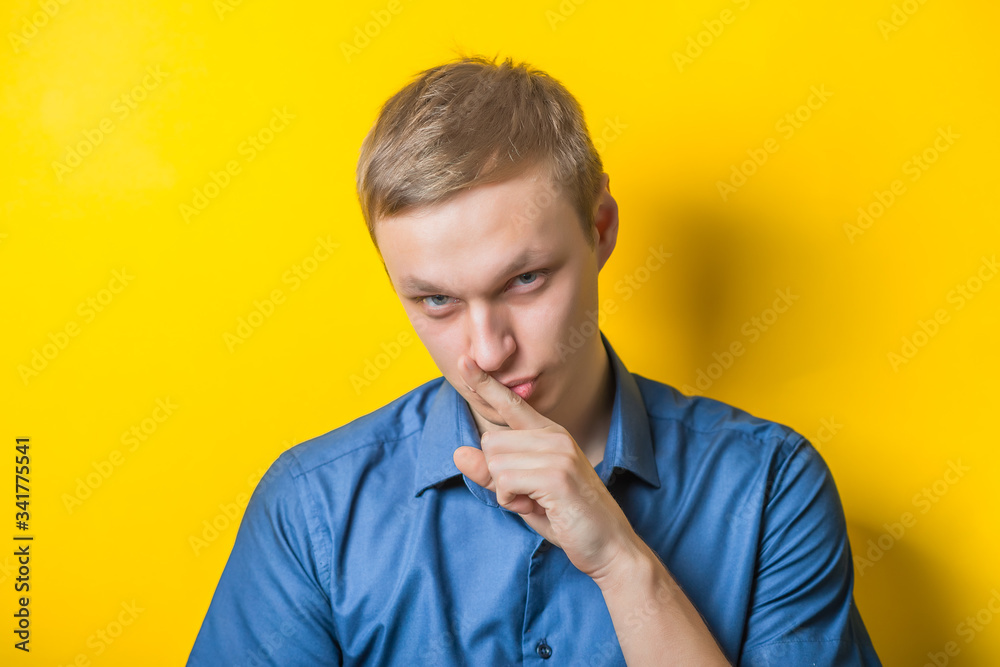 Blond young man holding his finger at the mouth, quiete, calme. Close portrait. Gesture. Isolated yellow background. photo Blond young man holding his finger at the mouth, quiete, calme. Close portrait. Gesture. Isolated yellow background. photo