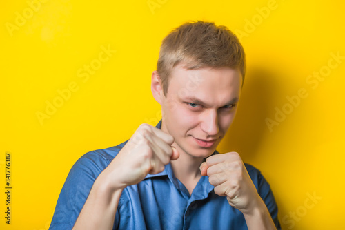 handsome elegant young man wearing a suit posing with fists up gesturing fight isolated on yellow