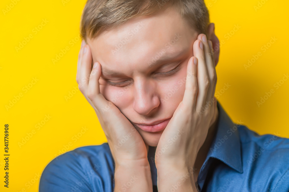 A young man close-up in a blue shirt on a yellow background, fall asleep. The guy wants to sleep. Gesture. Photos