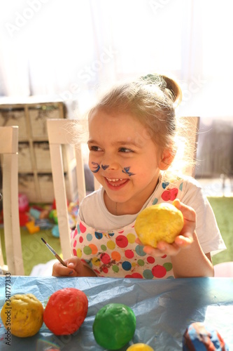 Cute girl with a brush for painting paints the salted dough pots at home. Creative creativity concept for children. Childhood. Normal quarantined life with coronavirus. Lifestyle COVID-19