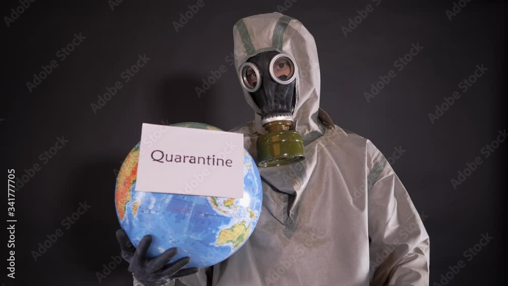 Man in a chemical protection suit and a gas mask. The guy is holding a model of the Earth, a globe. A placard with the following inscription is attached to the globe: QUARANTINE. Man in a chemical protection suit and a gas mask. The guy is holding a model of the Earth, a globe. A placard with the following inscription is attached to the globe: QUARANTINE.