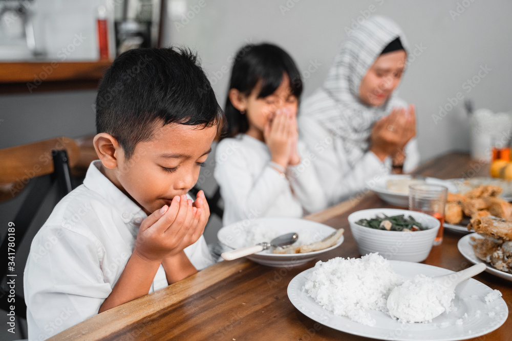 muslim family praying before eating their food. breaking the fast or iftar dinner muslim family praying before eating their food. breaking the fast or iftar dinner