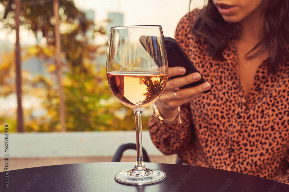 Beautiful elegant woman drinking wine and using cellphone outdoors.