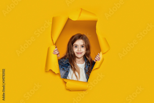 Portrait of cute happy smiling caucasian little cild girl raises clenched fists and poses in blue paper hole. © producer