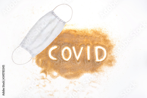 Sand on a white background. The inscription COVID on the hub, a protective mask around the sand and flip-flops. A vision of summer in 2020 during the Coronavirus pandemic. Summer in Covi-19
