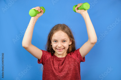 Fitness child. Portrait of a sporty girl with dumbbells on a blue background of the Studio. Training in the gym. Children's activity. Sport. Fitness, health and energy.