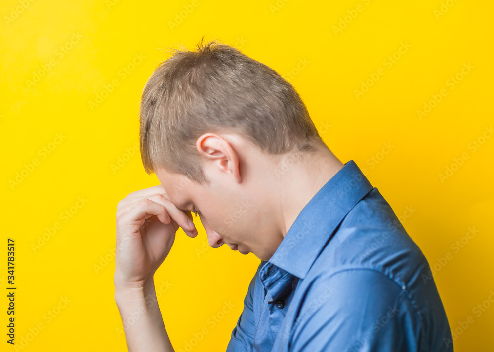 Young man in a blue shirt on a yellow background. showing fatigue two hand under head, anger, misunderstanding. gesture. photo shoot. Young man in a blue shirt on a yellow background. showing fatigue two hand under head, anger, misunderstanding. gesture. photo shoot.