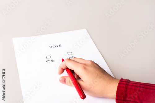 The person fills out the ballot paper. Voting during elections. The photo shows hands, a red pen and ballot paper.
