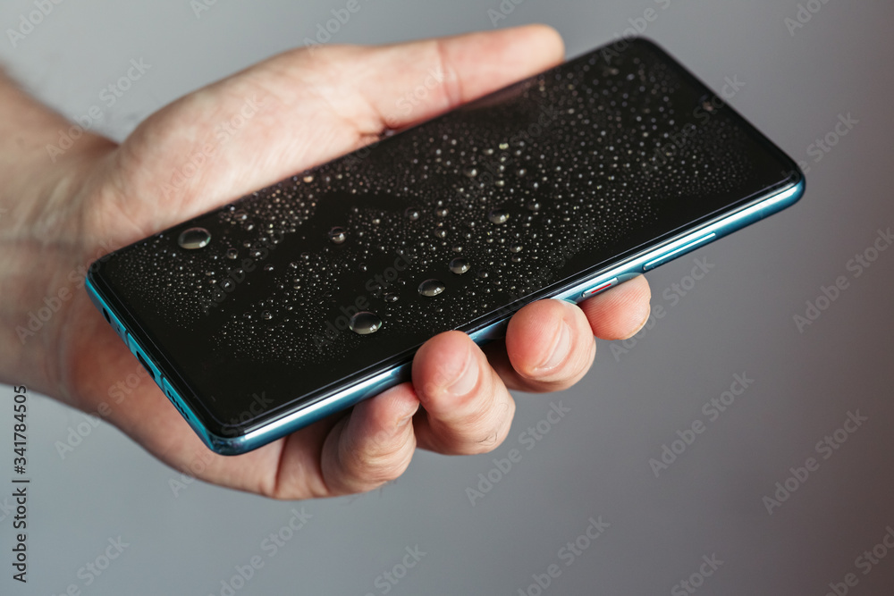 Drops on the glass of a smartphone screen, waterproof phone. man holds wet phone in his hand