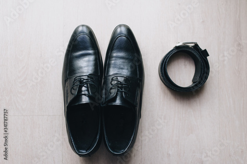 Black men's shoes for a businessman and a leather belt stand on the background of parquet. Photography, concept. Morning and preparation of the groom.