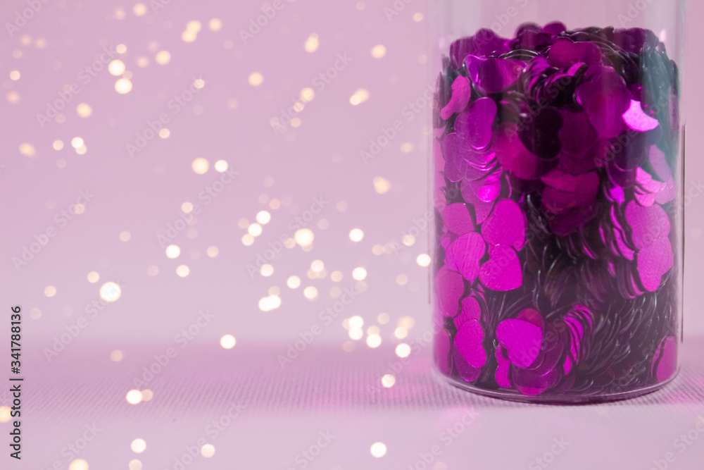 Glass bottle with purple heart shaped sparkles on pink background with copy space and blurred lights bokeh, defocused. Festive concept for your creative design - obrazy, fototapety, plakaty 