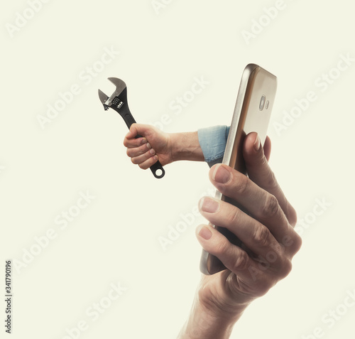 The human hand with black wrench stick out of a smartphone screen. Concept of technical support.