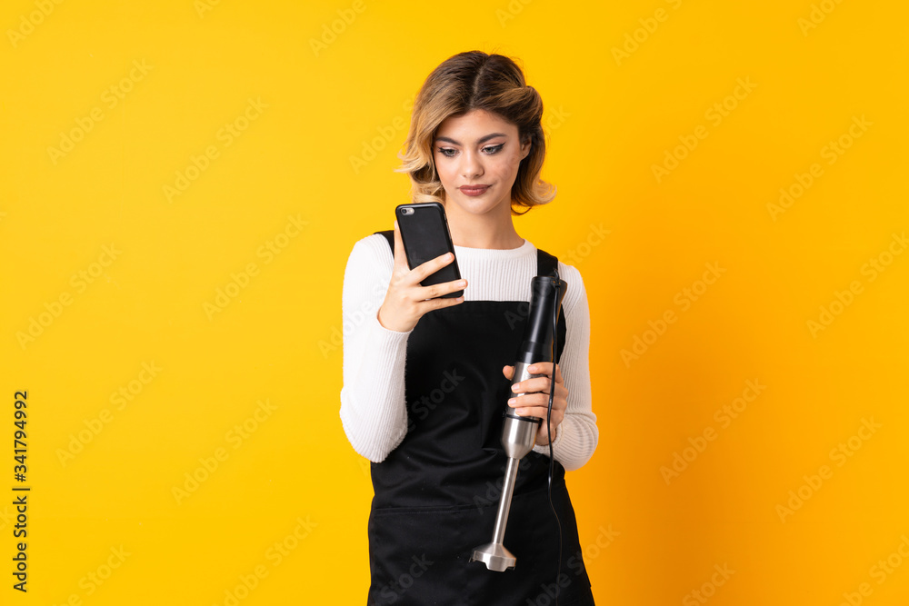 Girl using hand blender isolated on yellow background thinking and sending a message Girl using hand blender isolated on yellow background thinking and sending a message