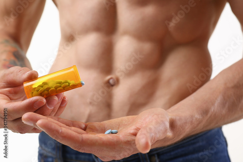 Fitness man pours pills from the jar into his hand intake of hormonal preparations for rapid growth of doping muscles to achieve high results is experiencing problems with potency after closeup