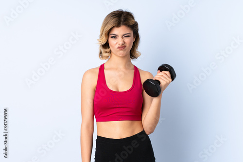 Teenager Russian girl making weightlifting isolated on blue background with sad expression