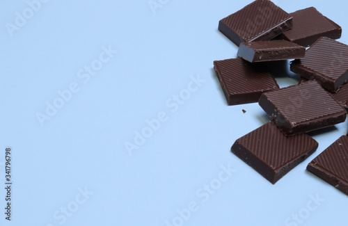a bar of dark chocolate is broken into pieces, lies on a blue background. Place for text, inscriptions. Sweet life, international chocolate festival, sugar addiction, consumption