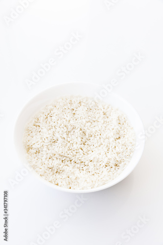 Raw dry rice in bowl isolated on white background, top view. Main asian food ingredient, natural food high in protein
