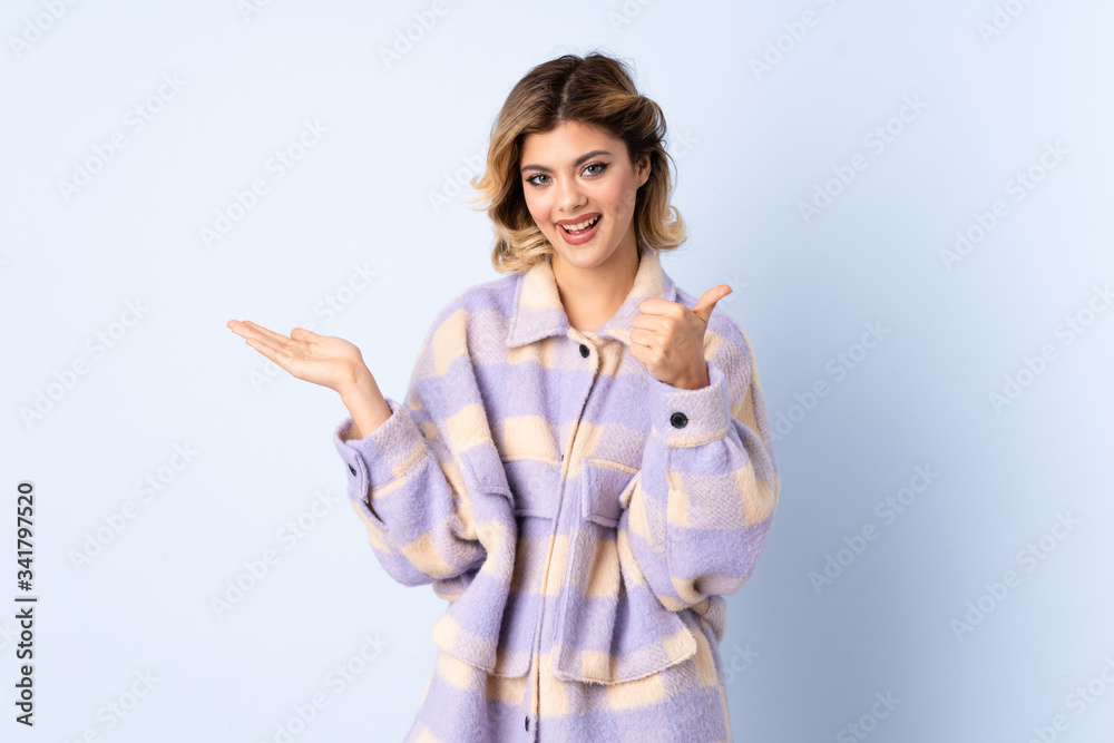 Young Russian woman isolated on blue background holding copyspace imaginary on the palm to insert an ad and with thumbs up Young Russian woman isolated on blue background holding copyspace imaginary on the palm to insert an ad and with thumbs up