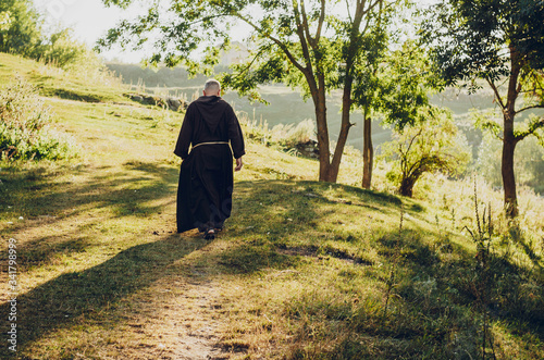 monk of the Capuchin Order, an adult wise man with a beard and in long dark brown clothing walks the stone path in the morning in nature