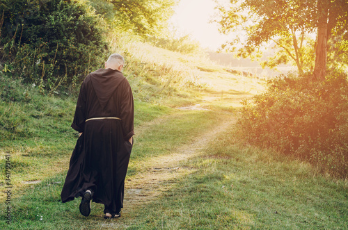 monk of the Capuchin Order, an adult wise man with a beard and in long dark brown clothing walks the stone path in the morning in nature