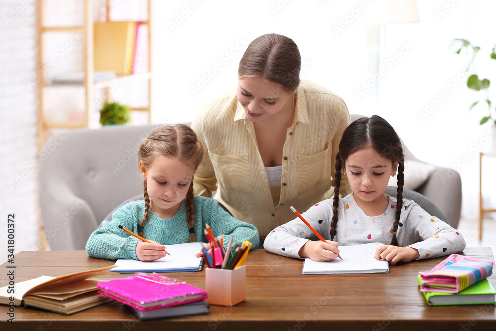 Mother helping her daughters with homework at table indoors Mother helping her daughters with homework at table indoors
