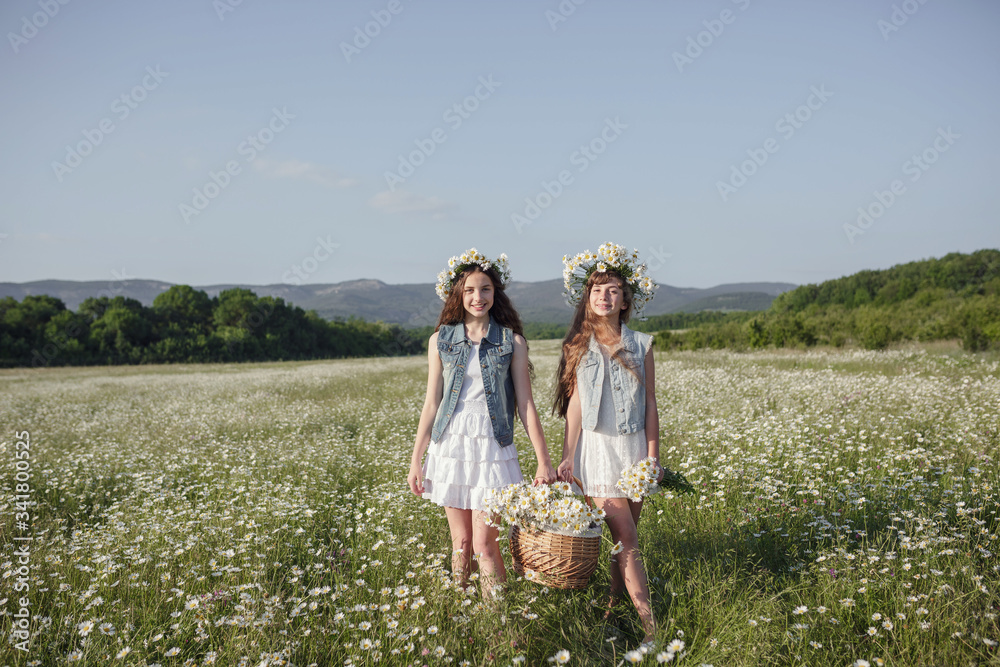 two cute teen girls in denim overalls walk in a daisy field two cute teen girls in denim overalls walk in a daisy field