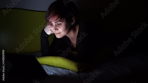Young woman watching online tv show in bed at night. People hooked up with entertainment devices before going to bed. technology and leisure concept. Lifestyle at home for young people.