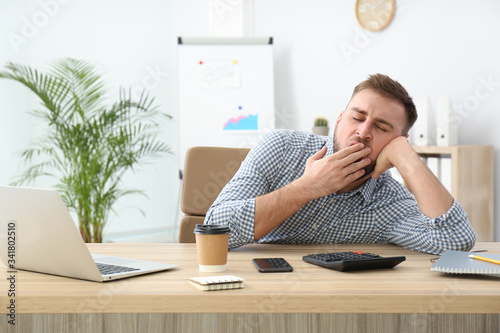 Lazy young office employee yawning at workplace