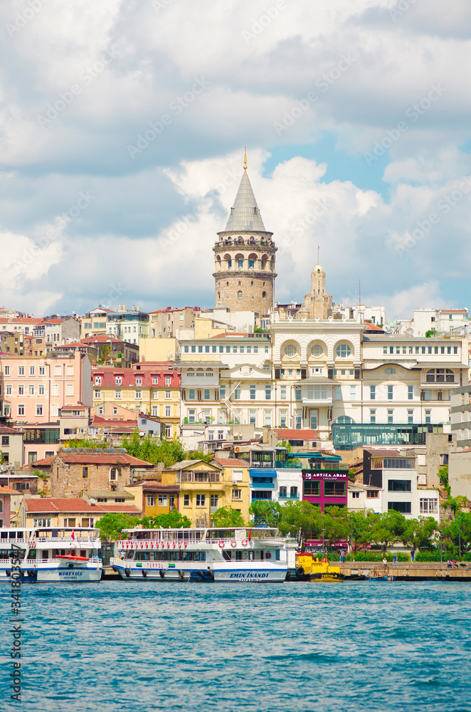Obraz premium Galata Tower. View of famous historic landmark across Golden Horn. Galata bridge with fishermen. Popular tourist destination. Cloudy. Clear blue water. Turkey, Istanbul