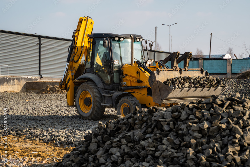 Obraz premium Yellow wheel loader Excavator machine working at construction site with gravel. Preparing of the fundament for a asphalting. Road construction site. Building of a parking.
