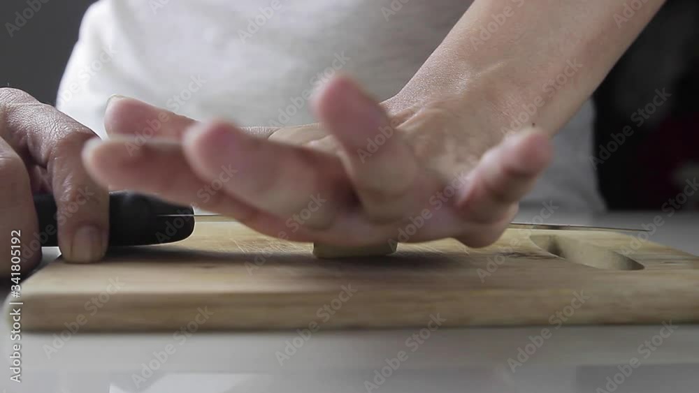 Closeup of a woman's hand crushing a garlic clove with knife on a wooden board Closeup of a woman's hand crushing a garlic clove with knife on a wooden board