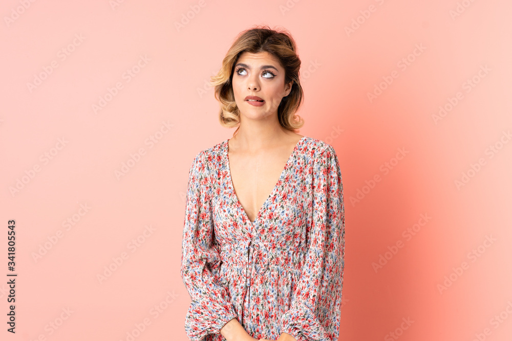 Young Russian woman isolated on pink background having doubts while looking up