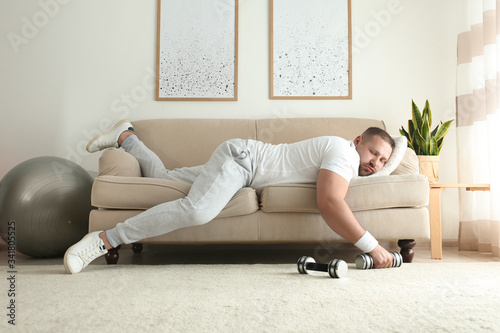 Lazy overweight man with dumbbells sleeping on sofa at home