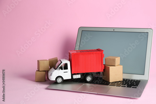 Laptop, truck model and carton boxes on pink background. Courier service