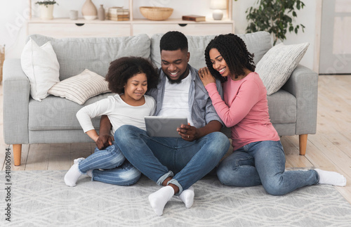 Happy Black Parents And Little Daughter Using Digital Tablet At Home