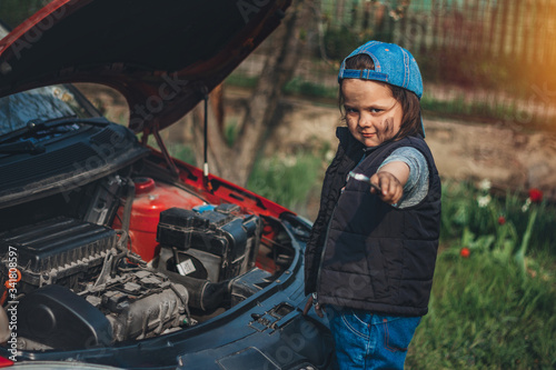 Little child trying to fix broken real car. Dreaming to be auto technician