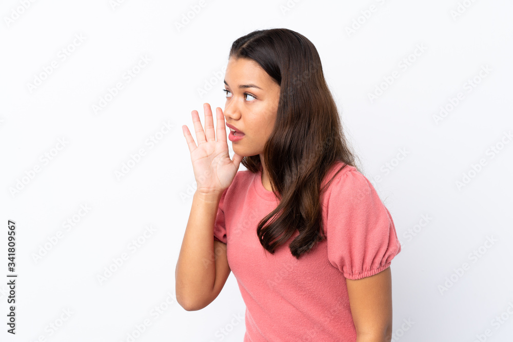 Young Colombian girl over isolated white background shouting with mouth wide open to the lateral Young Colombian girl over isolated white background shouting with mouth wide open to the lateral