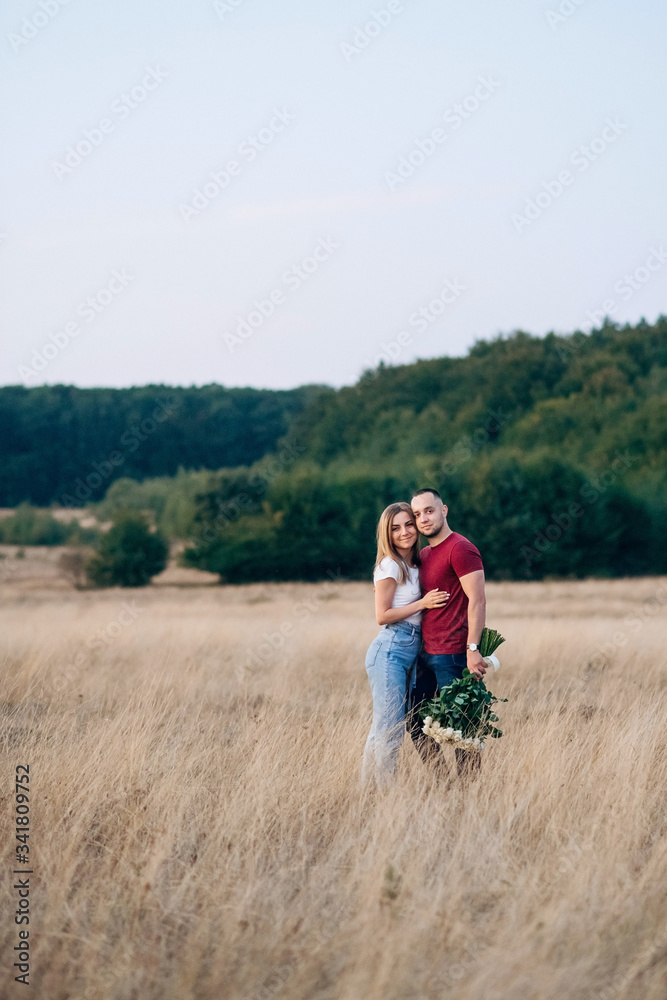 Romantic attractive couple in love staying in the wide field and looking to each other. Handsome strong man with gorgeous bouquet of white roses hugging his attractive woman after proposal of marriage