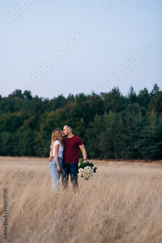 Romantic attractive couple in love staying in the wide field and kissing. Handsome strong man with gorgeous bouquet of white roses kiss his attractive woman after proposal of marriage