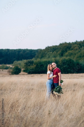 Romantic attractive couple in love staying in the wide field and looking to each other. Handsome strong man with gorgeous bouquet of white roses hugging his attractive woman after proposal of marriage