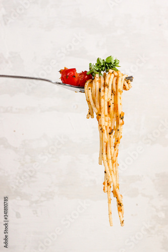 Spagetti pasta over fork with fresh tomato and fresh basil, photographed on a light background photo