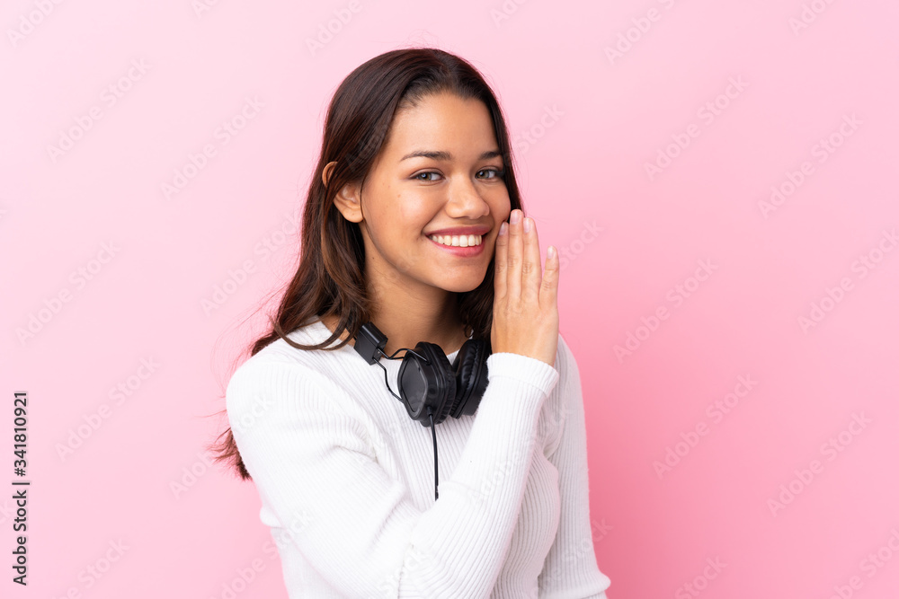 Young woman with earphones over isolated pink wall whispering something Young woman with earphones over isolated pink wall whispering something
