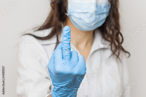 Stop SARSCoV, virus 2020, chinese virus COVID-19. Womens hand in blue medical gloves show middle finger or fuck. Concept of protection against HIV. Doctor in blue medical gloves and protective mask