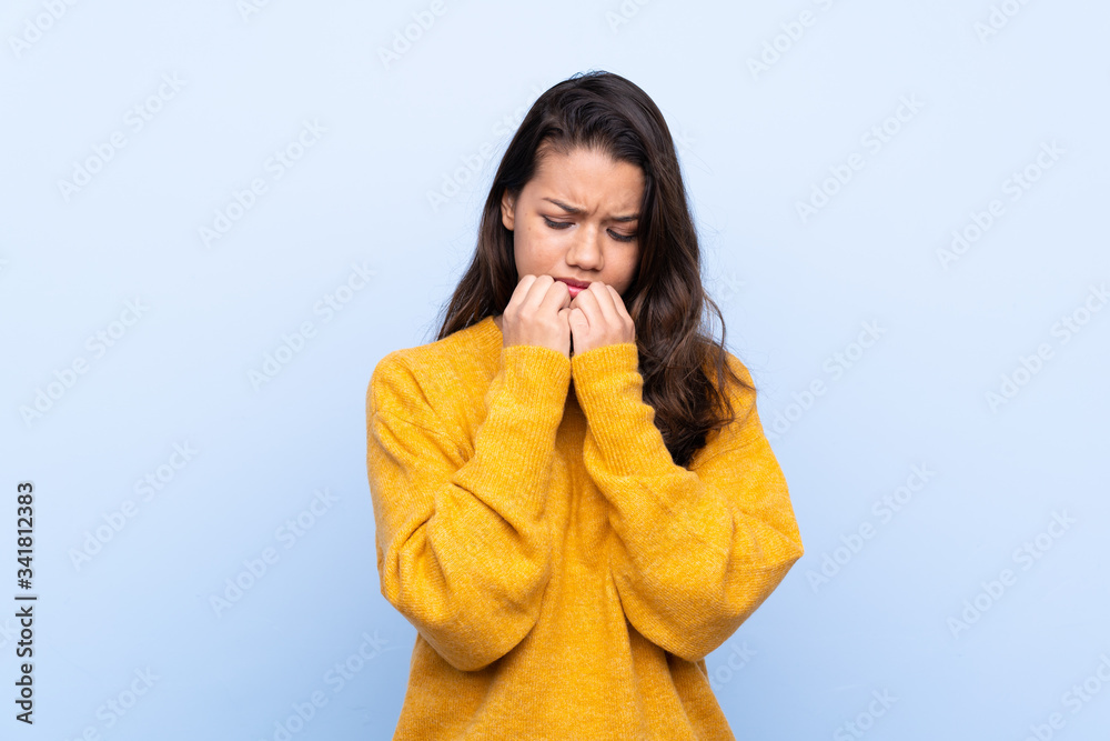 Young Colombian girl with sweater over isolated blue background nervous and scared putting hands to mouth Young Colombian girl with sweater over isolated blue background nervous and scared putting hands to mouth