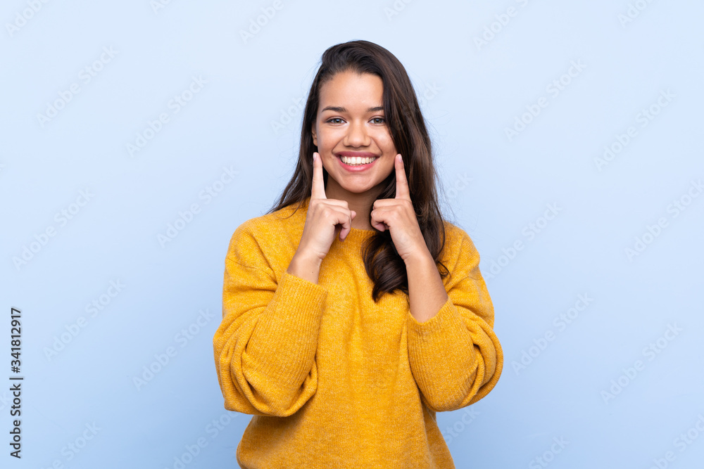 Young Colombian girl with sweater over isolated blue background smiling with a happy and pleasant expression Young Colombian girl with sweater over isolated blue background smiling with a happy and pleasant expression