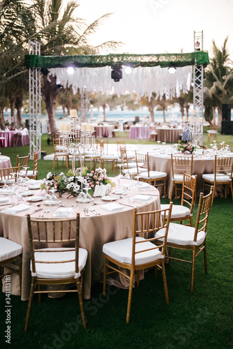 International Wedding outdoor celebration party under palm trees. Served tables on green area in hotel. Landyard. Beige and pink colors. Close-up and wide angle.